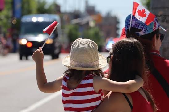 Family waving Canadian flags at a Canada Day parade